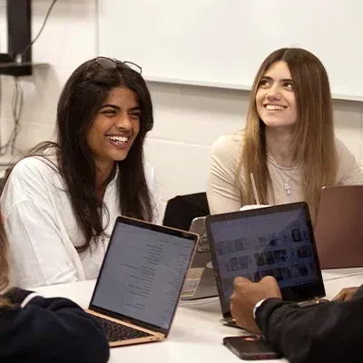 两个女大学生拿着笔记本电脑坐在桌边笑个不停